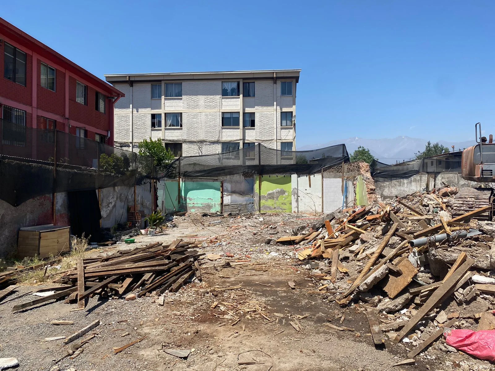 Acopio de madera y escombros de una demolición residencial junto a edificios vecinos con malla de protección